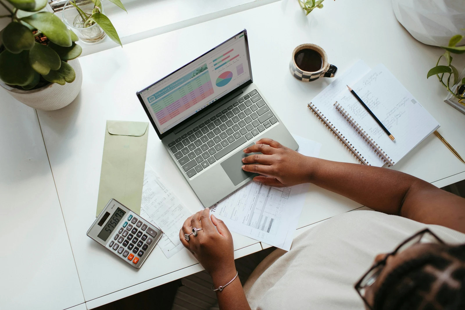 Small business owner at a laptop with a calculator, working out costs on a notepad